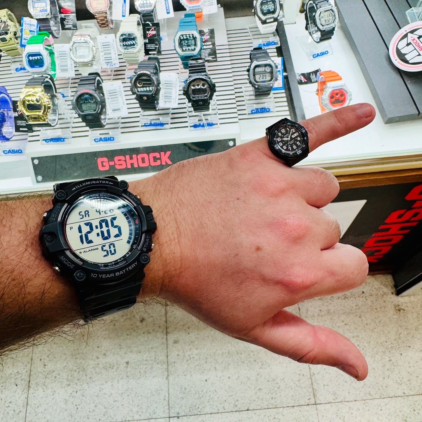 Casio AE-1500 worn beside a matching Casio watch ring in a retail display