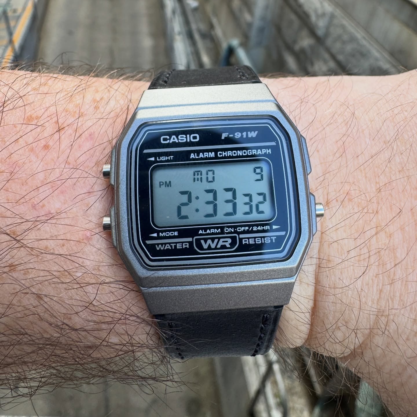 Close view of a gunmetal Casio F-91W on a black leather strap worn outdoors
